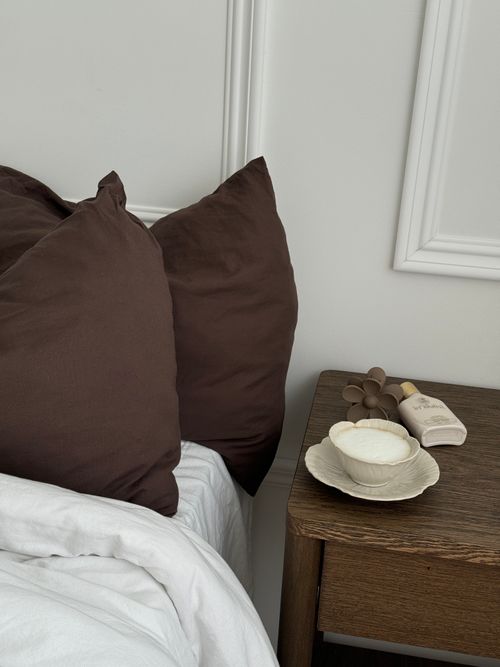 Free A cozy bedroom scene featuring brown pillows, a nightstand with a bowl, and skincare items. Stock Photo