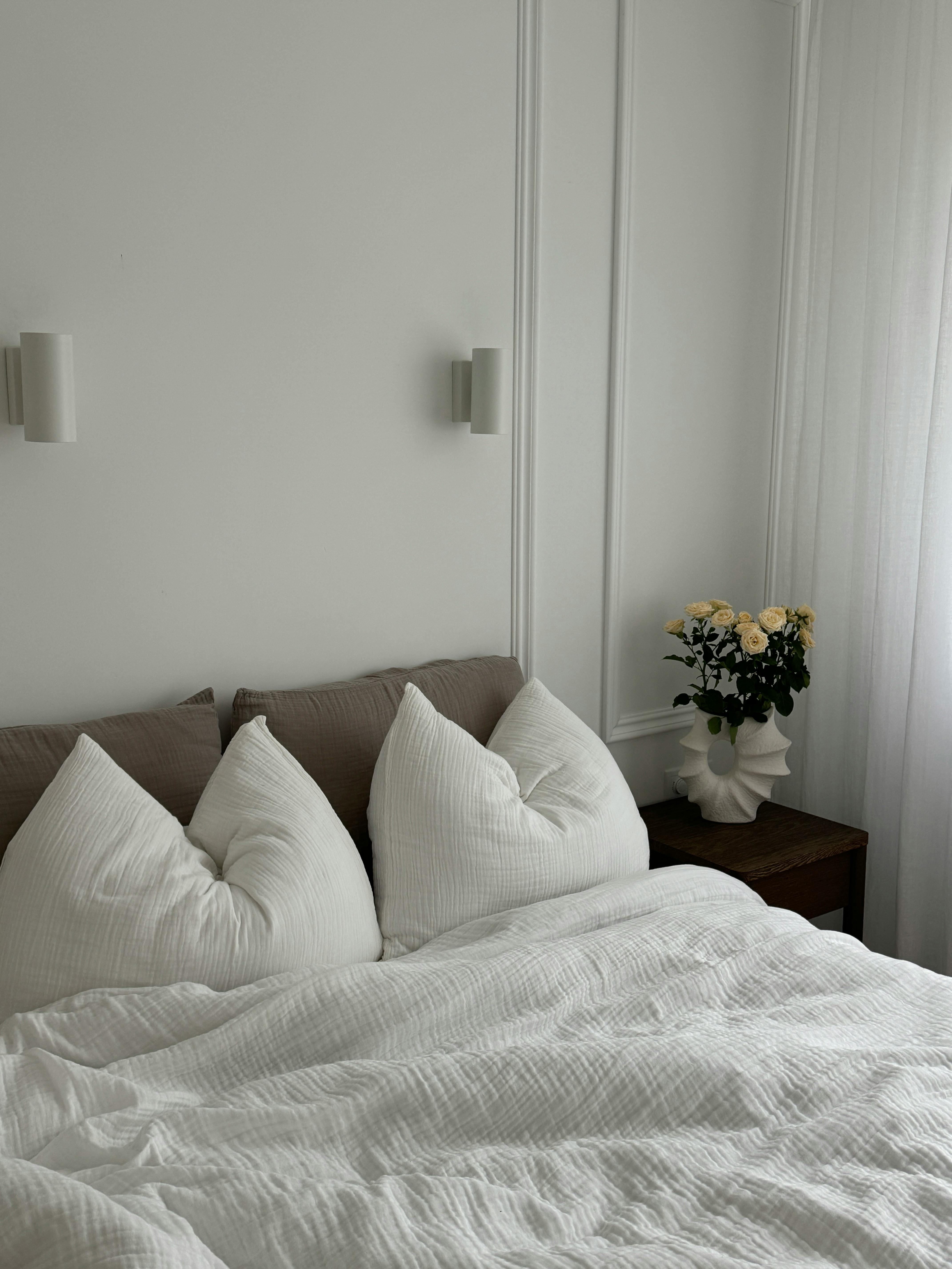 Elegant bedroom interior with white pillows and flowers, evoking tranquility.