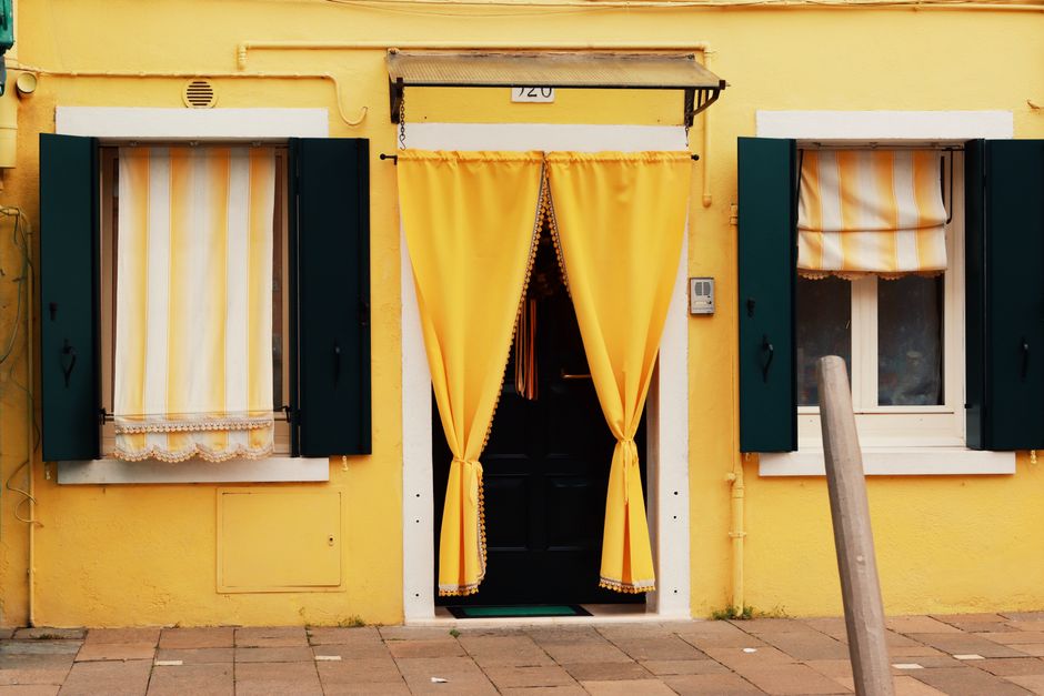 Charming yellow house with green shutters and curtains in Venice, Italy, showcasing classic Venetian architecture.