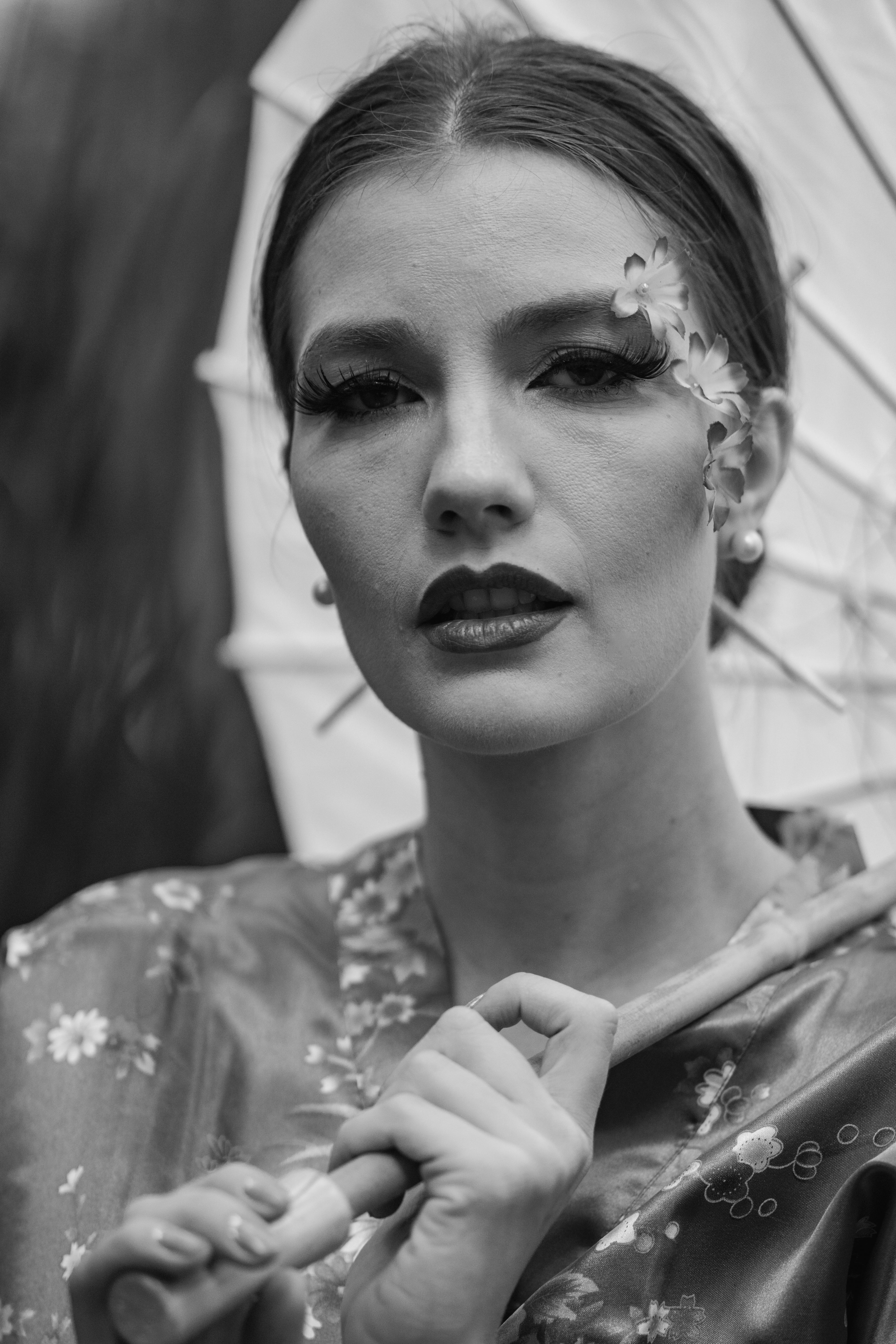 Black and white portrait of an elegant woman with an umbrella, in traditional attire, showcasing artistic makeup.