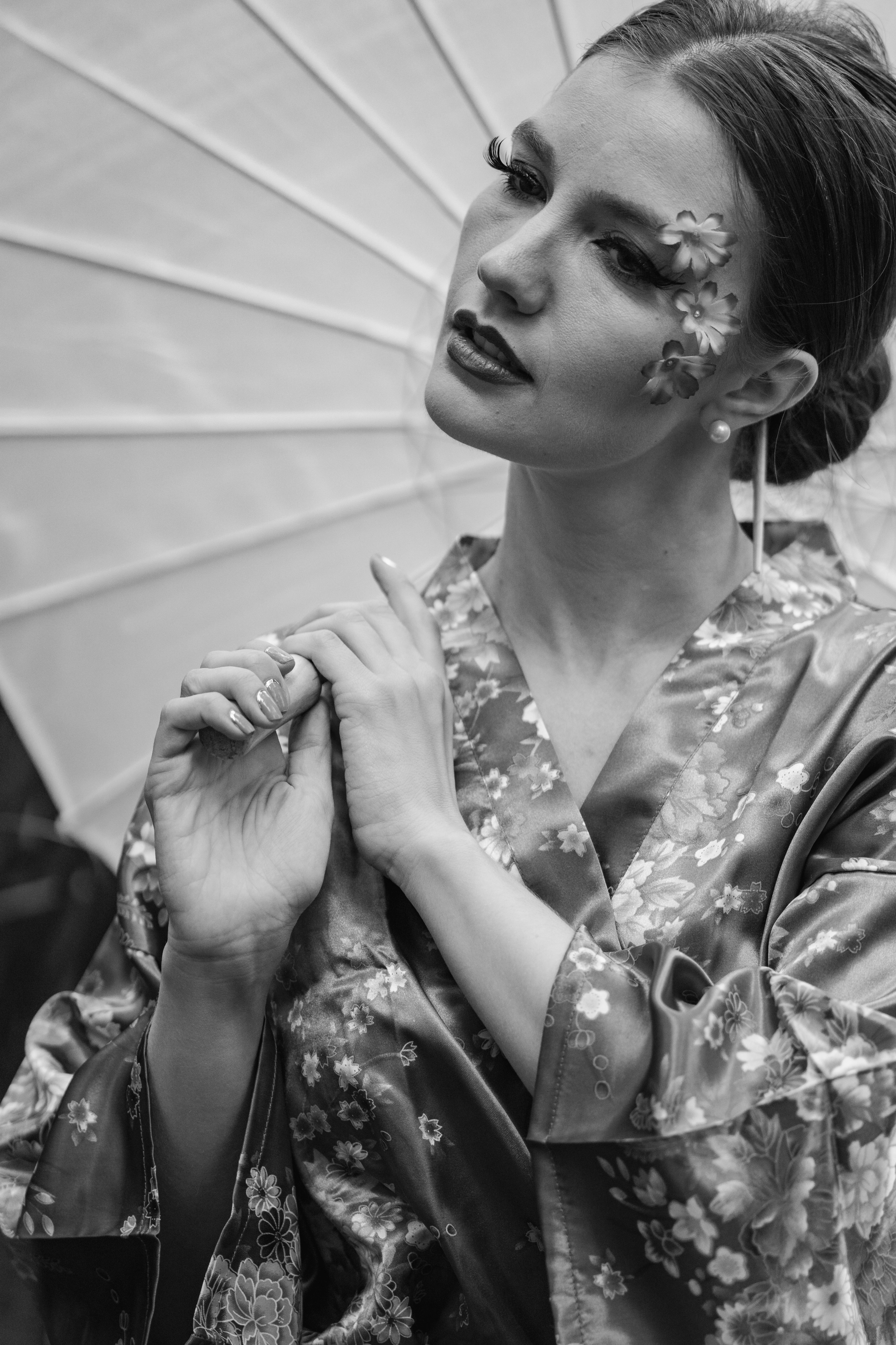 Black and white portrait of a woman in a kimono with creative floral makeup and holding an umbrella.