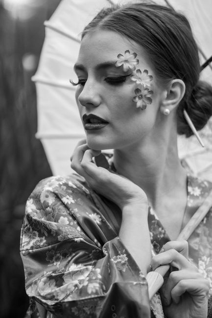 Monochromatic portrait of a woman in traditional attire with artistic floral face makeup holding an umbrella.