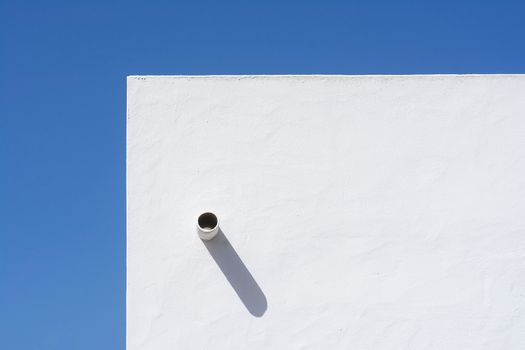 A minimalist white wall casting a distinct shadow under a clear blue sky, showcasing modern architectural design.