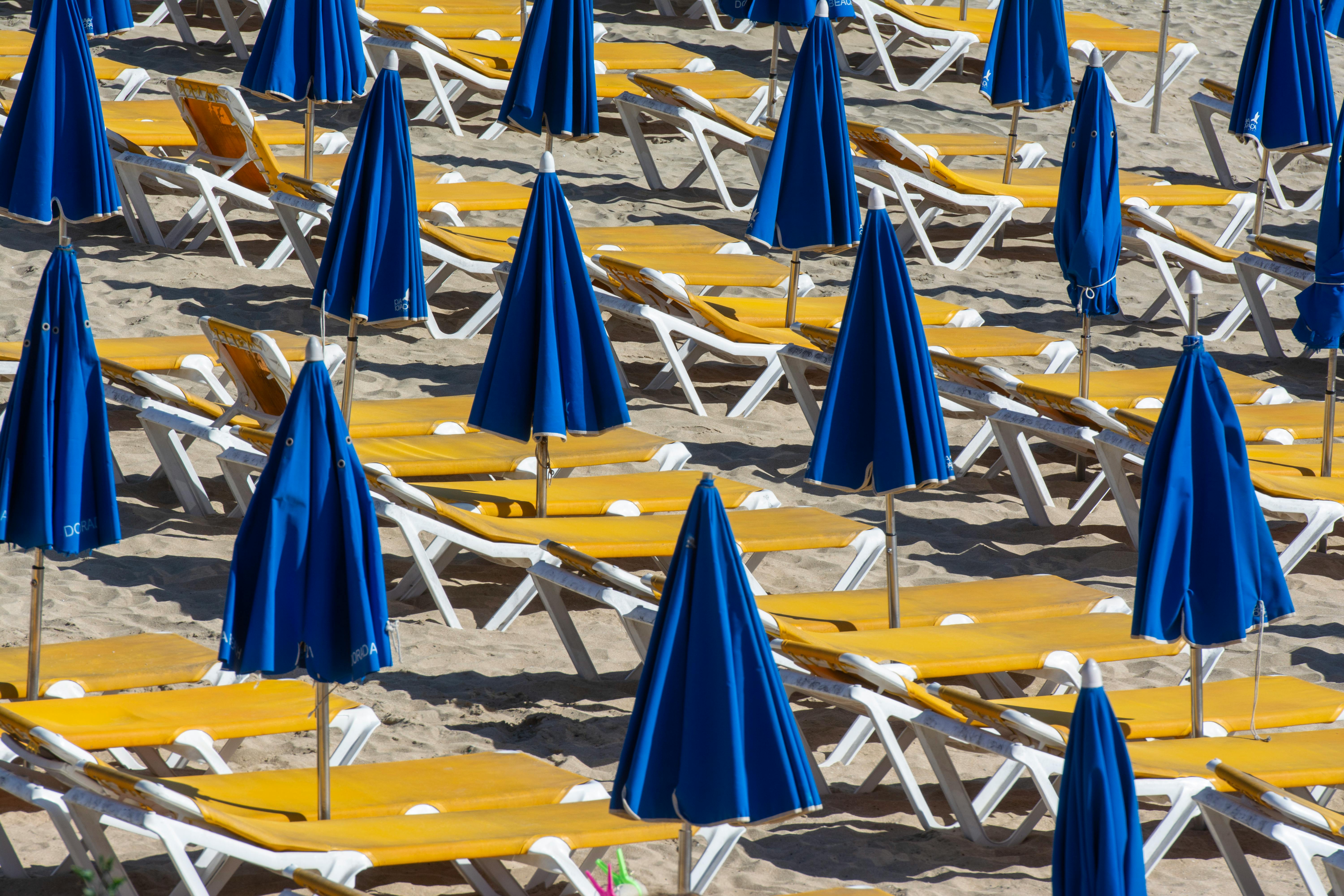 Empty sun loungers with blue umbrellas on a sunny beach, ideal for vacation and travel themes.