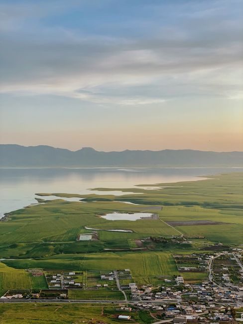 Breathtaking aerial panorama of Qurago, Iraq, showcasing lush greenery and calm lake at sunset.