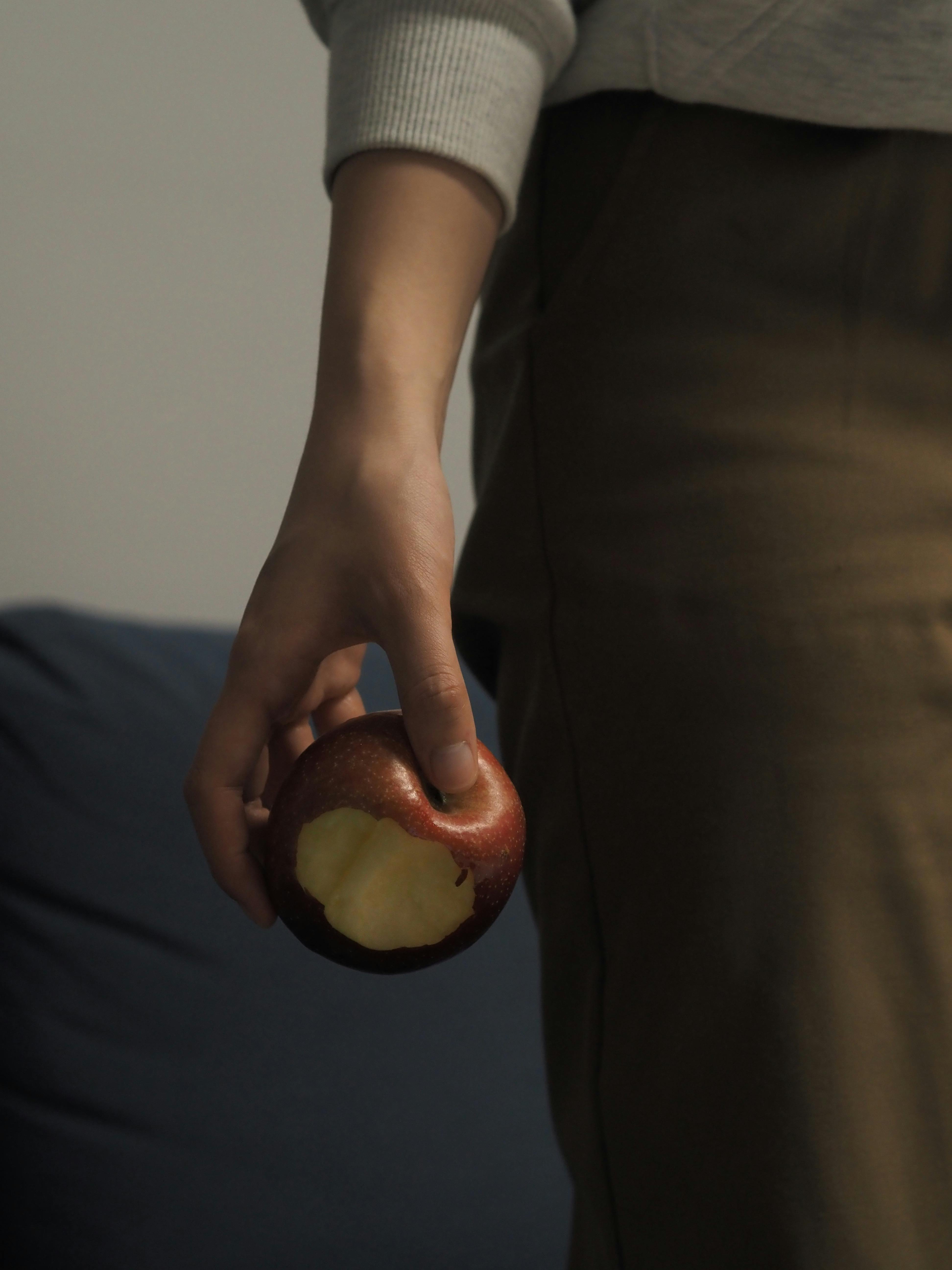 Close-up of a person holding a bitten red apple indoors, depicting health and lifestyle.
