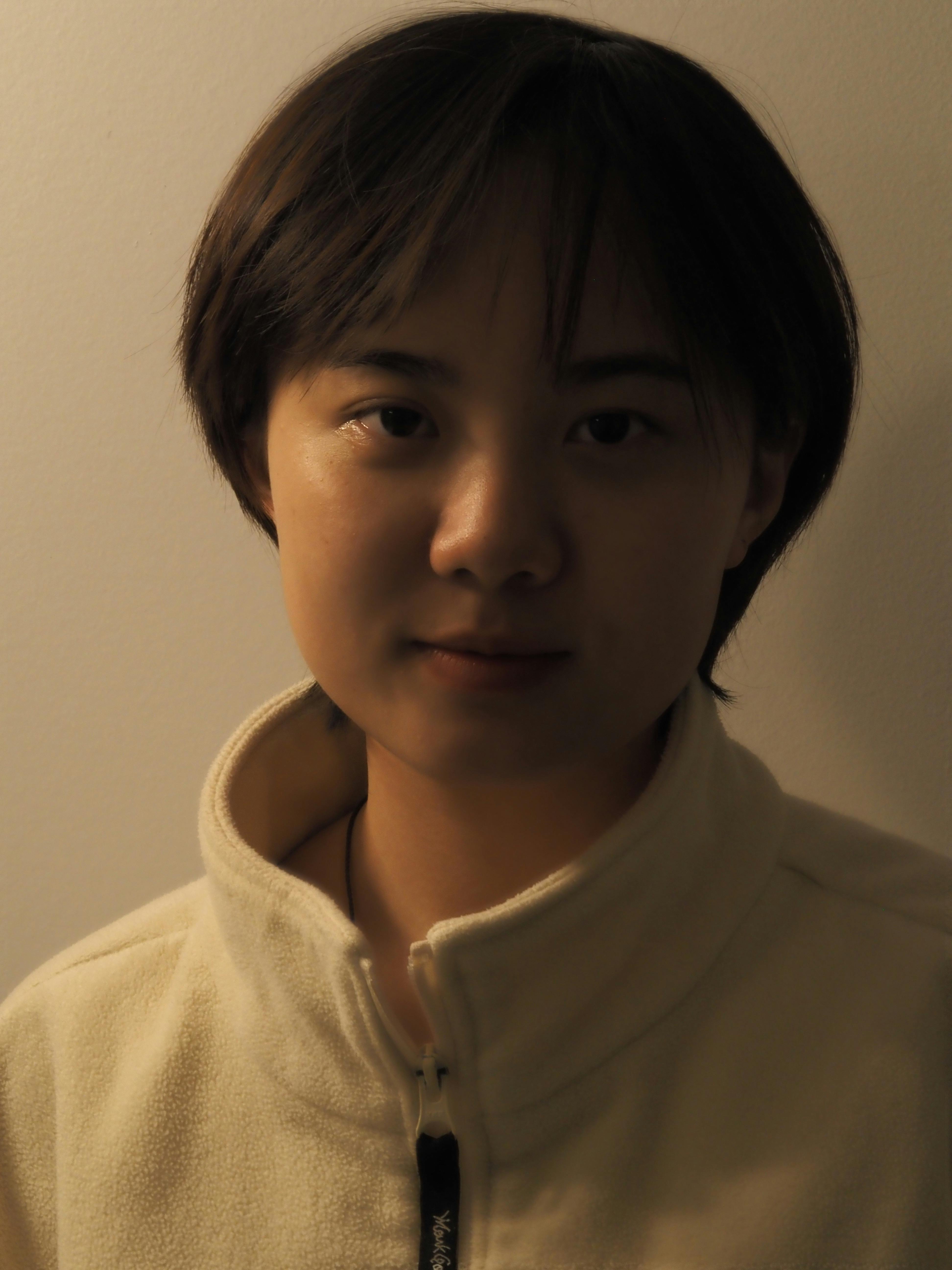 Warm-toned indoor portrait of a young adult against a simple backdrop.