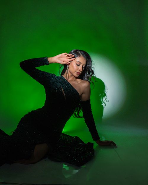 Free A woman in a sparkling black gown poses gracefully against a vibrant green background. Stock Photo