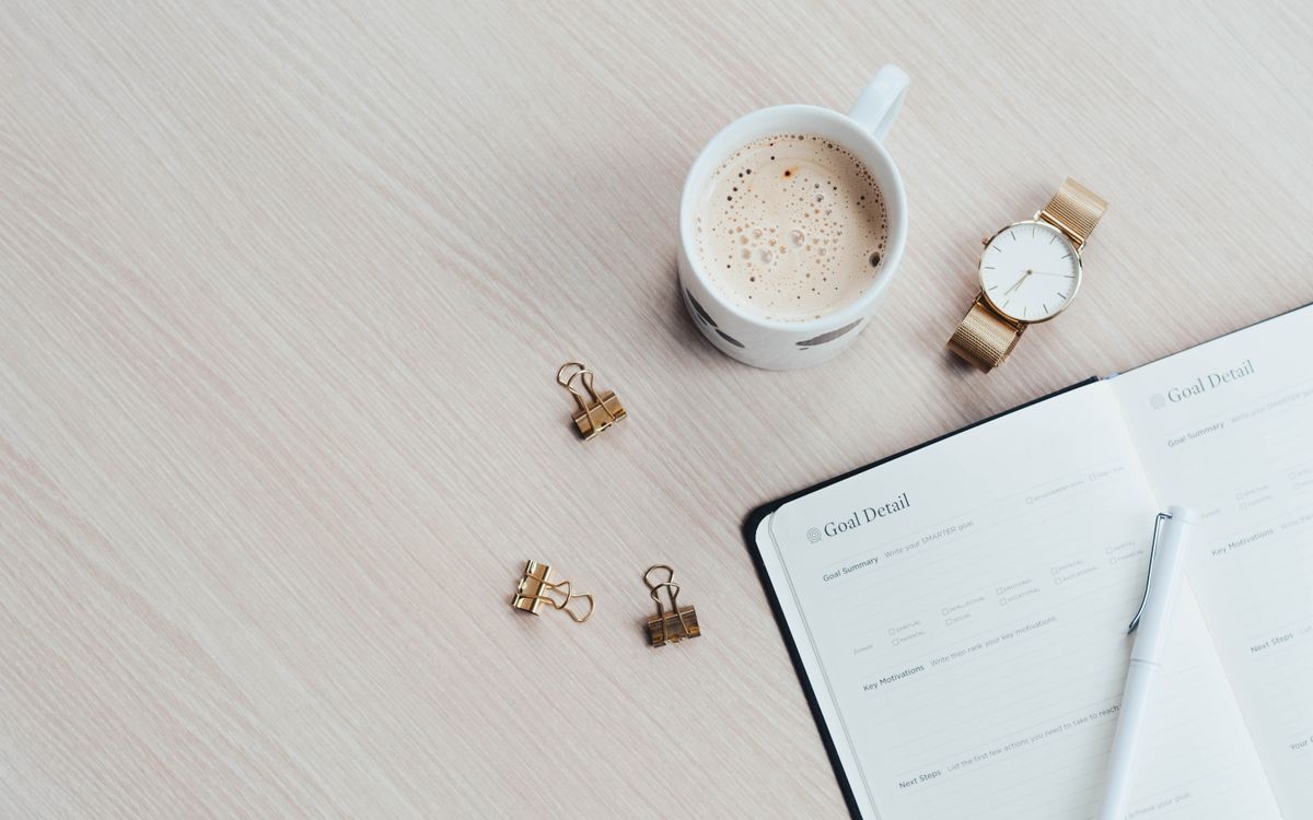 A minimalist desk arrangement featuring a coffee cup, notebook, pen, and wristwatch.
