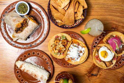 Savor a delicious spread of authentic Mexican tacos, burrito, and refreshing drink on rustic wood table.