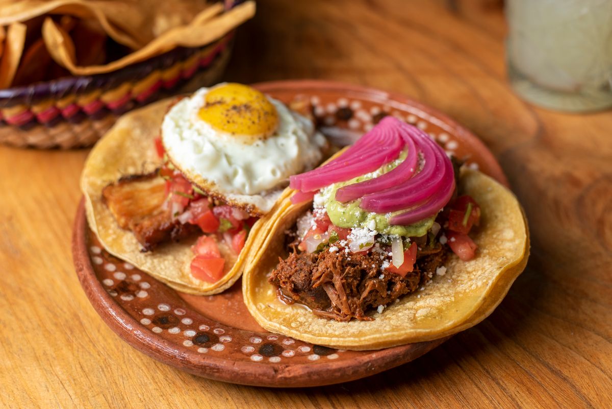 Two corn tortilla tacos with fried egg, shredded pork, guacamole and pickled onion