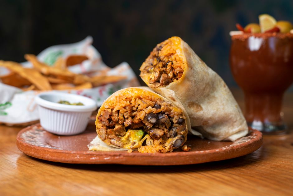 A carne asada burrito cut in half on a cutting board, showing grilled steak, rice, black beans, melted cheese, and pico de gallo inside a flour tortilla.