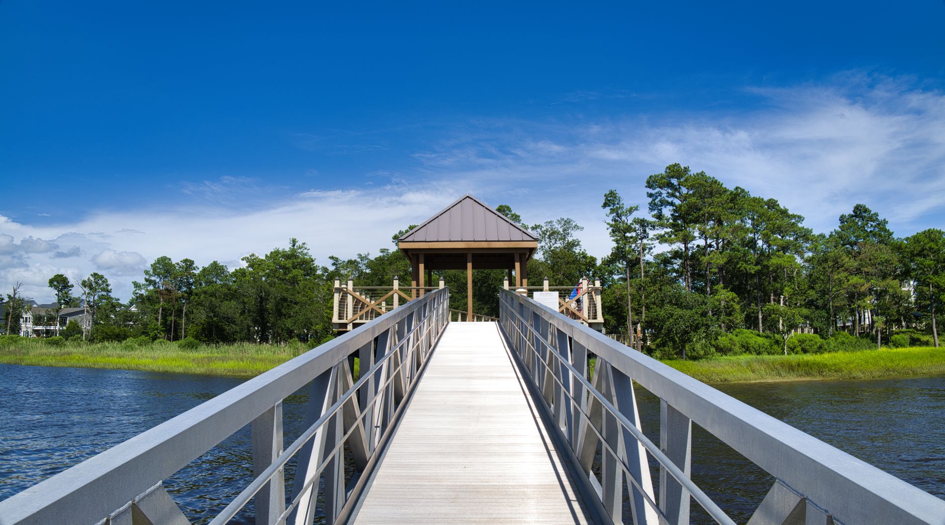 Beautiful wooden boardwalk leading to a gazebo over water in Wilmington, NC with lush greenery.