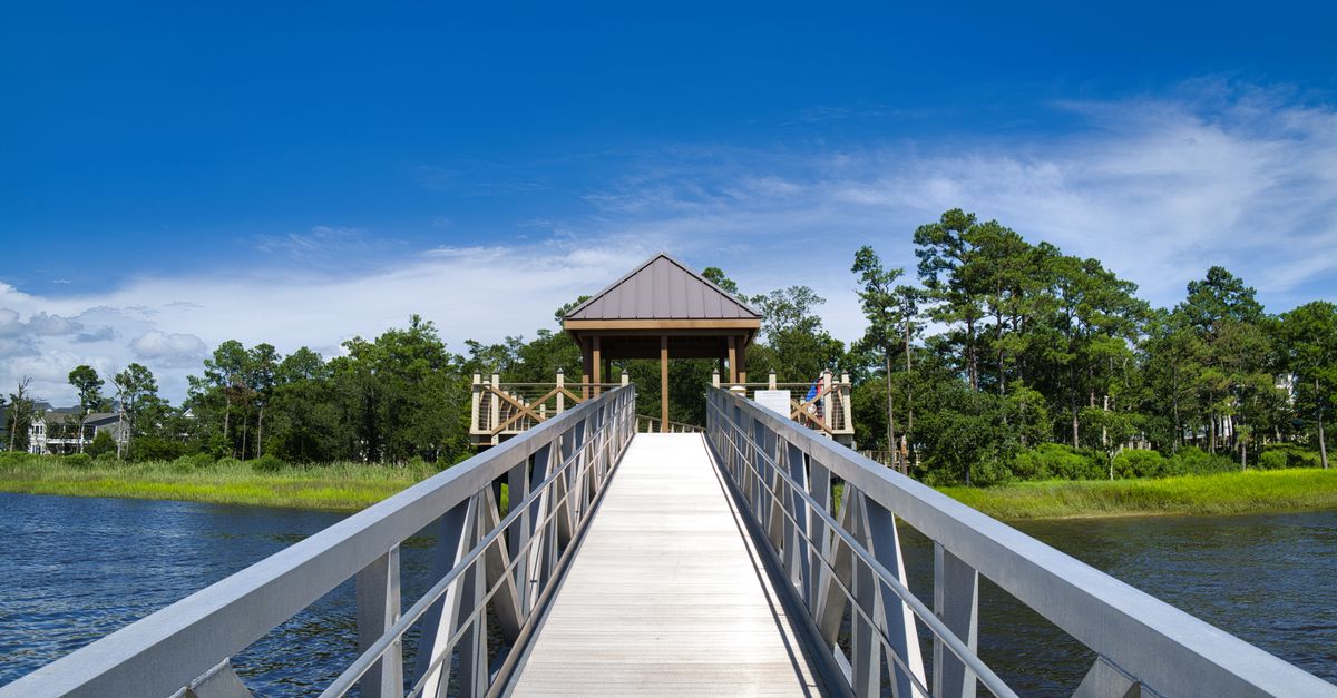 Beautiful wooden boardwalk leading to a gazebo over water in Wilmington, NC with lush greenery.