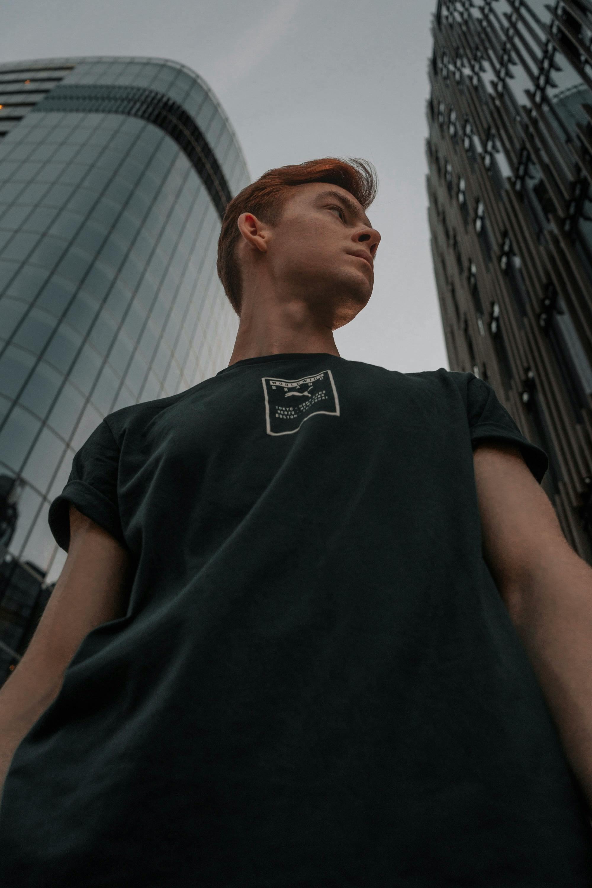 一位男模特在城市摩天大楼间低角度时尚摆姿的肖像