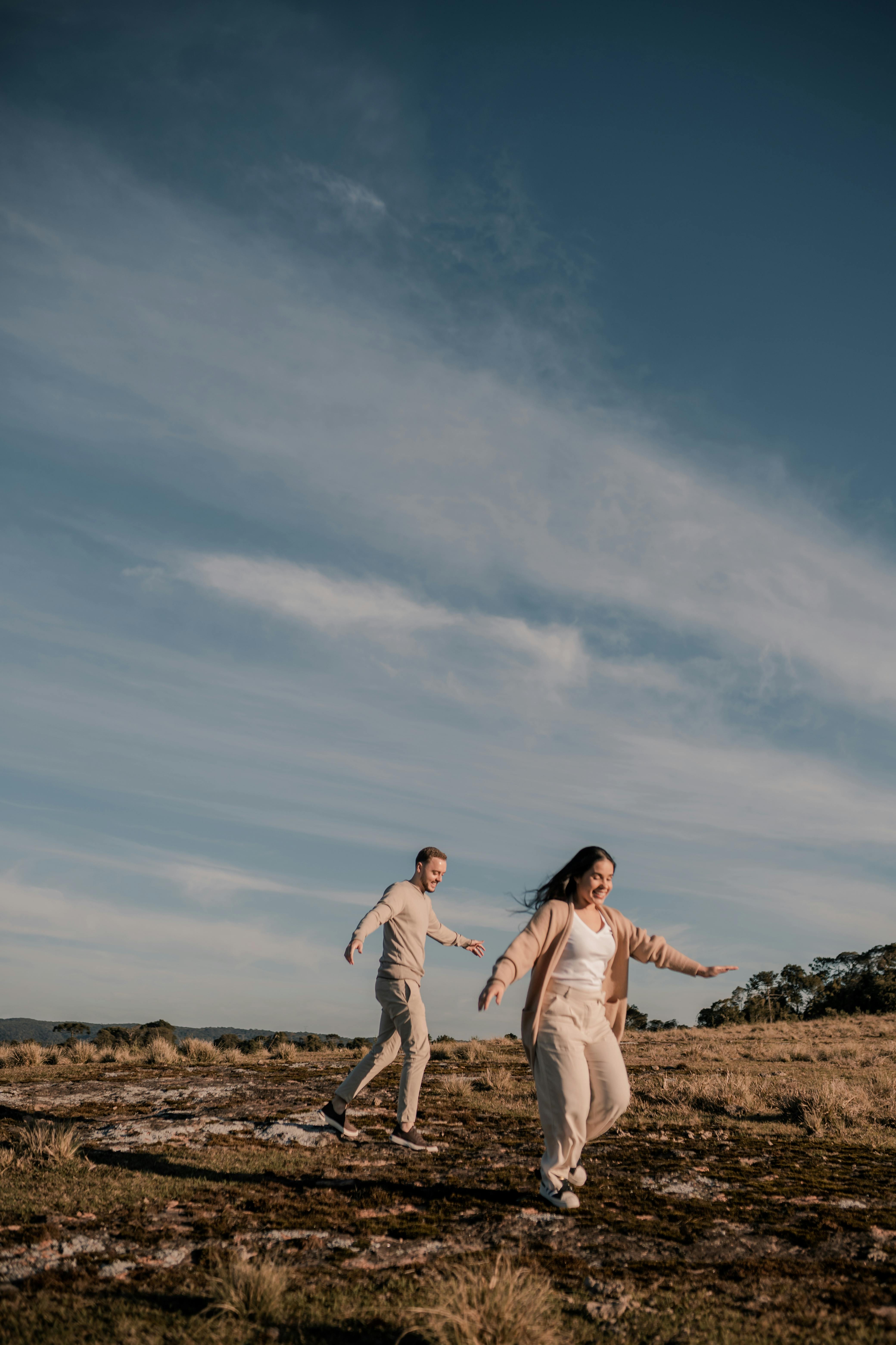 A happy couple runs freely in a sunny open field, embracing love and togetherness.