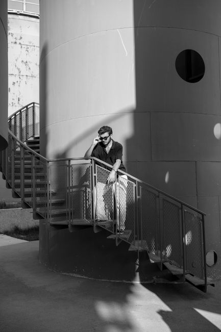 Black and white photo of a man standing on an industrial staircase in an urban setting.
