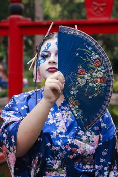A colorful portrait of a person in a traditional geisha costume holding a decorative fan.