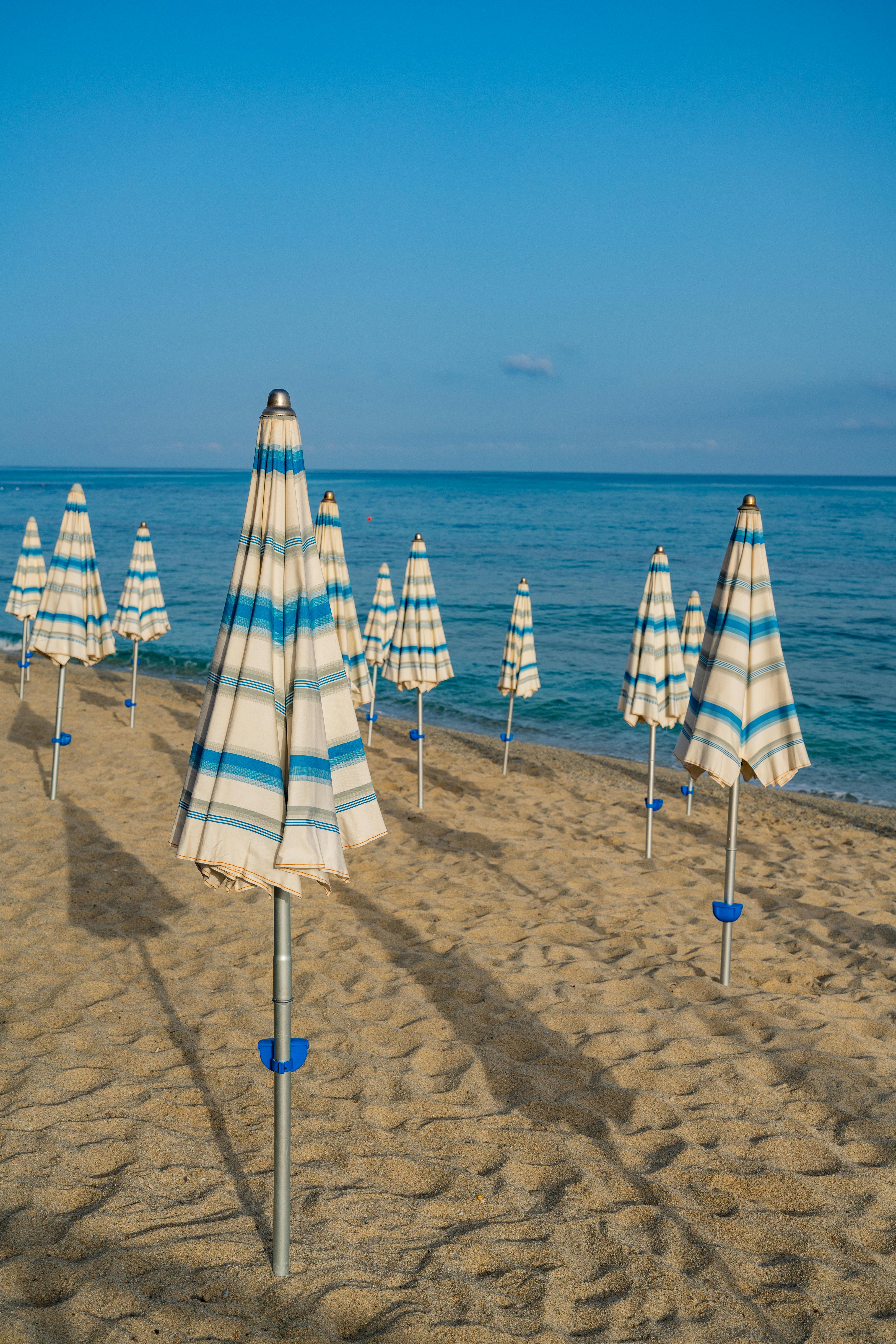 A tranquil scene featuring striped umbrellas on a sandy beach in Scilla, Italy.
