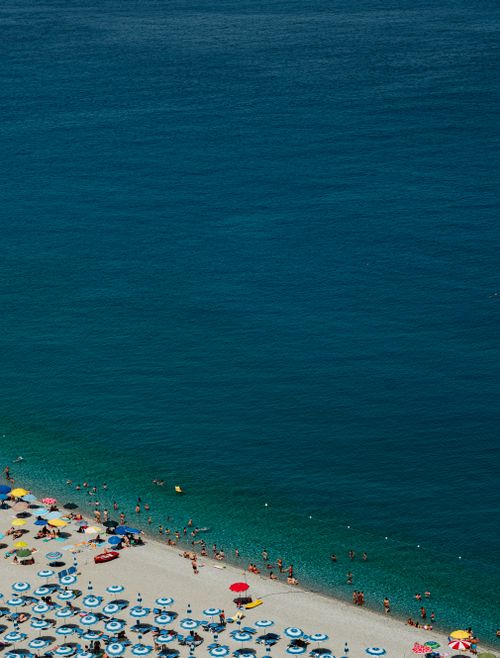 Free Vibrant summer scene of Scilla's beach with umbrellas and swimmers in clear blue waters. Stock Photo