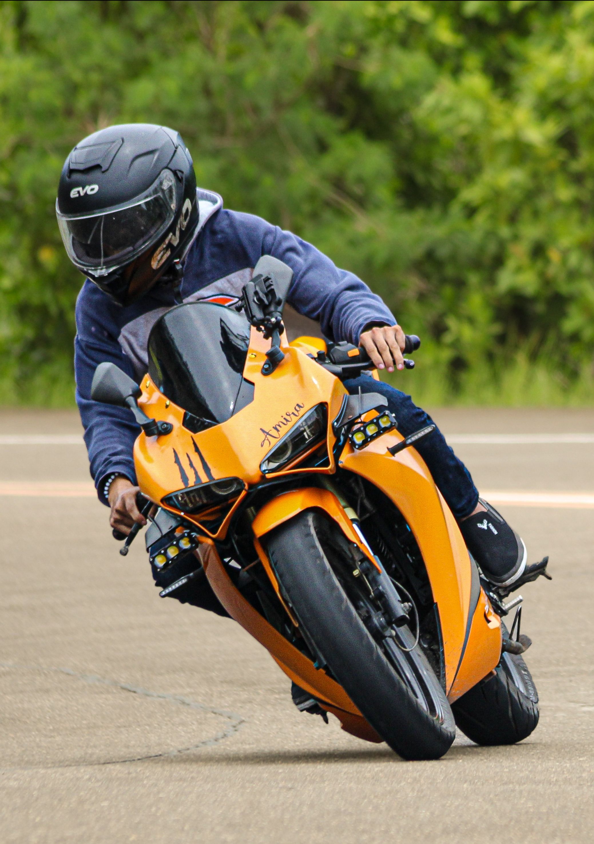 A biker in full gear leans into a curve on an orange sport motorcycle during a race.
