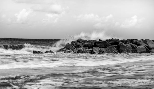 Black and white image of ocean waves crashing against rocky shore, creating a moody seascape.