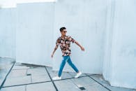 一位穿着时尚花卉衬衫和牛仔裤的男士走在户外，散发着自信的气息