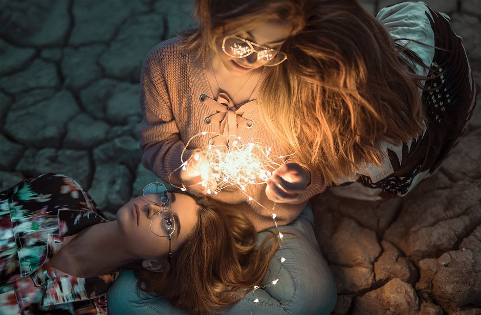 Two fashionable young women adorned with fairy lights, creating a warm and dreamy atmosphere.