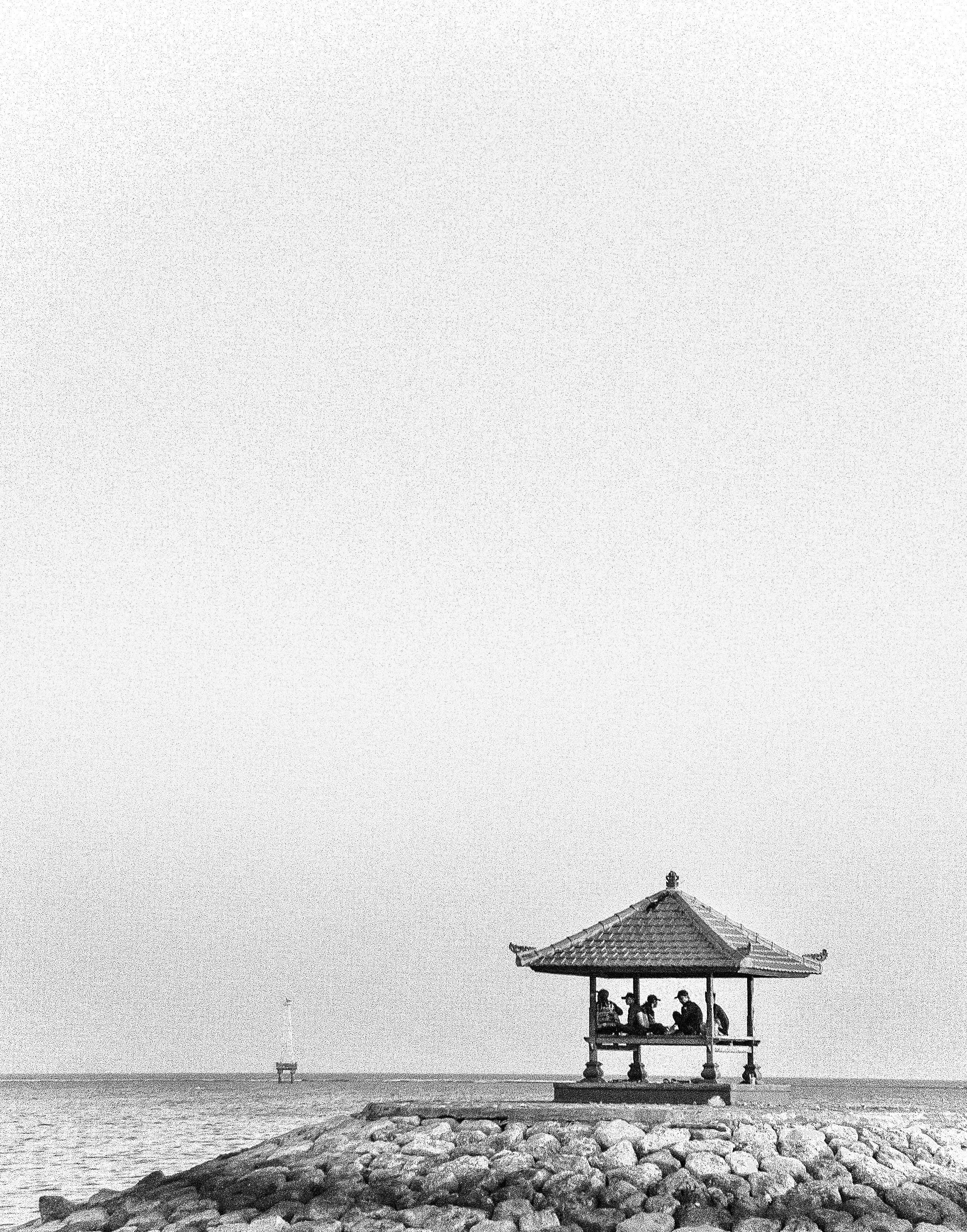 A minimalist black and white photo of a pagoda by the sea with people inside, creating a serene landscape.