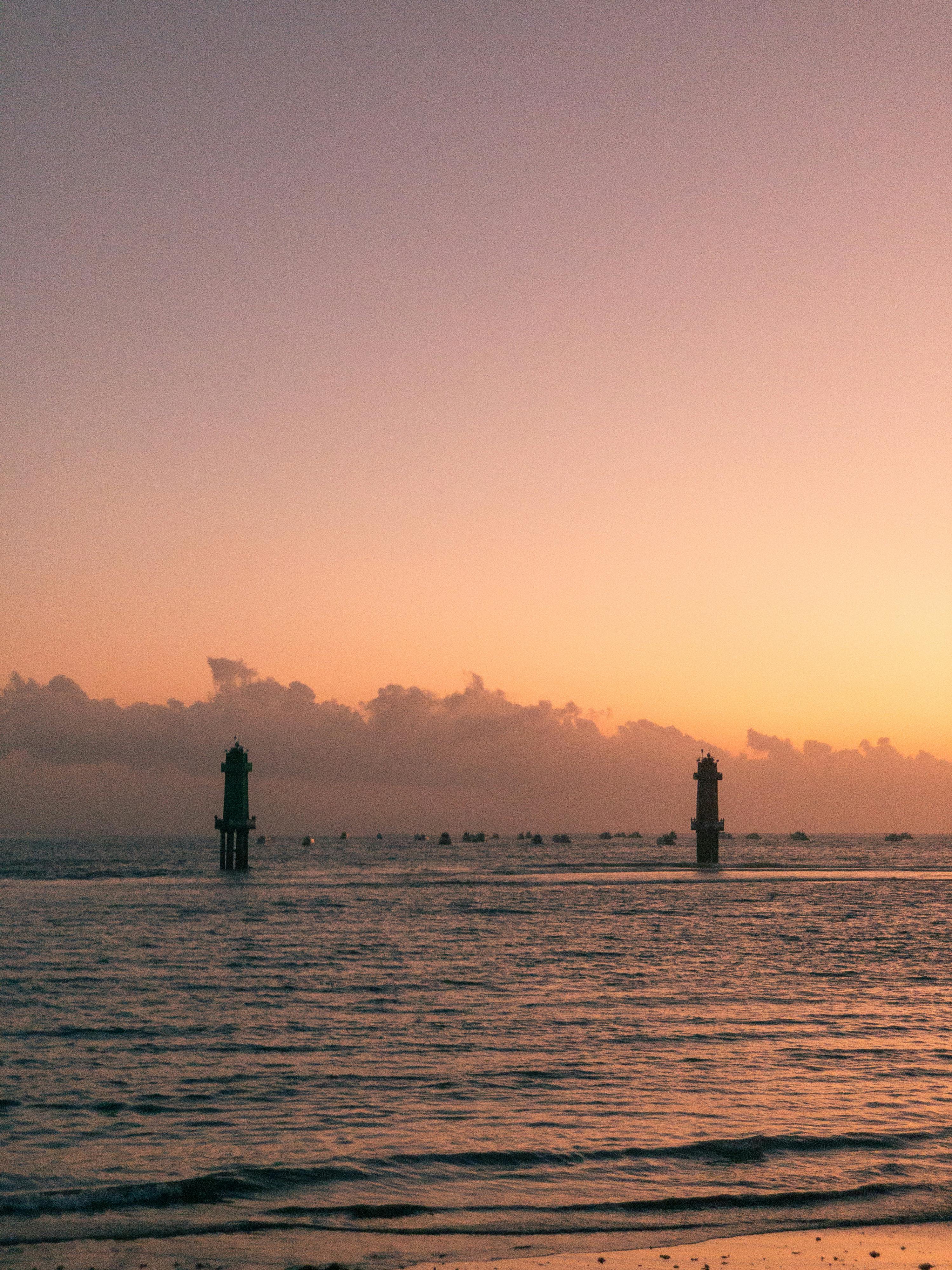 A calming sunset scene featuring two distant lighthouses over the tranquil ocean.