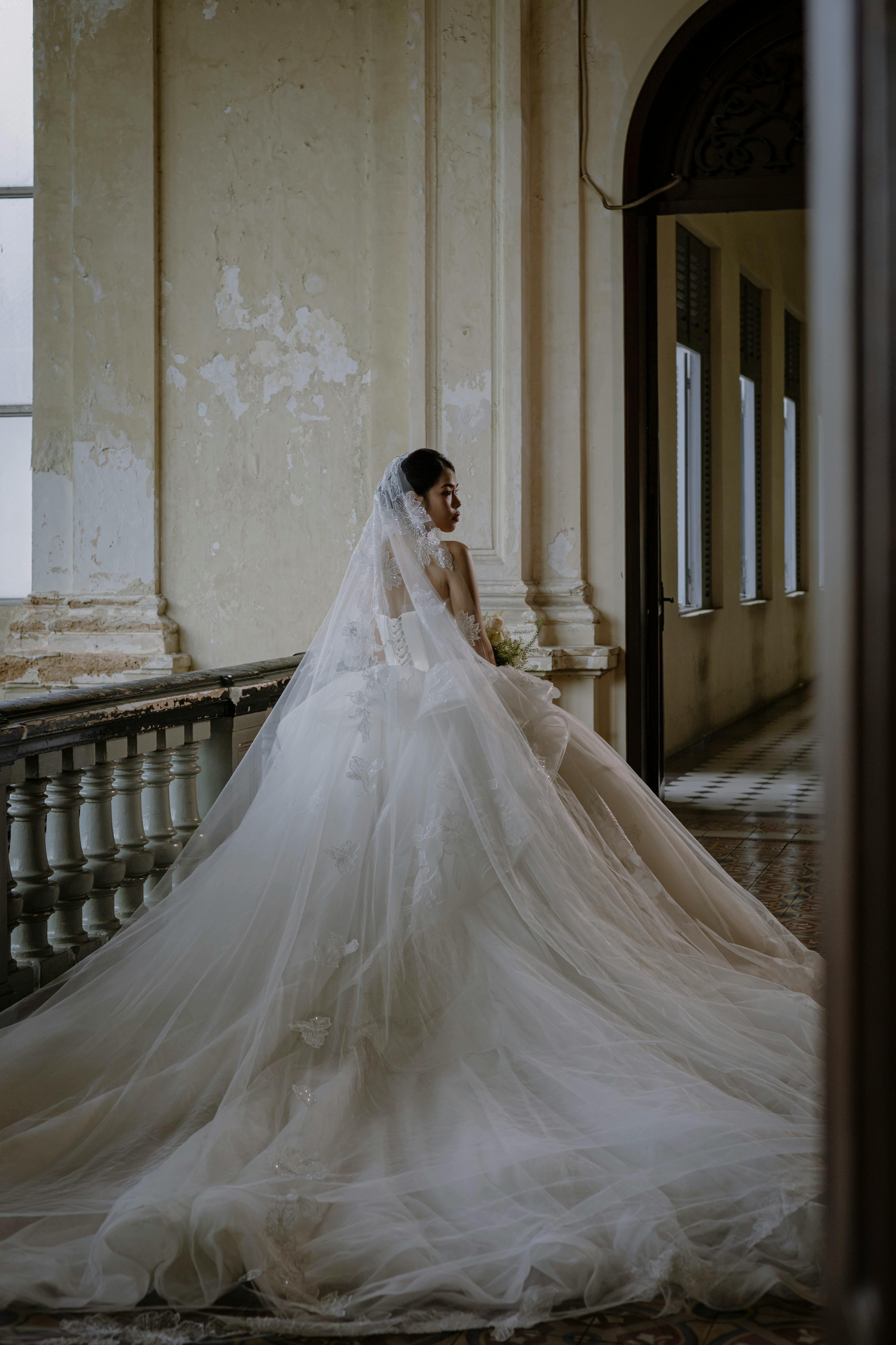 Bride in white gown on a balcony exudes timeless elegance in a vintage setting.