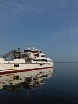 A large white yacht with red accents sits calmly on the still ocean, reflecting the clear blue sky.