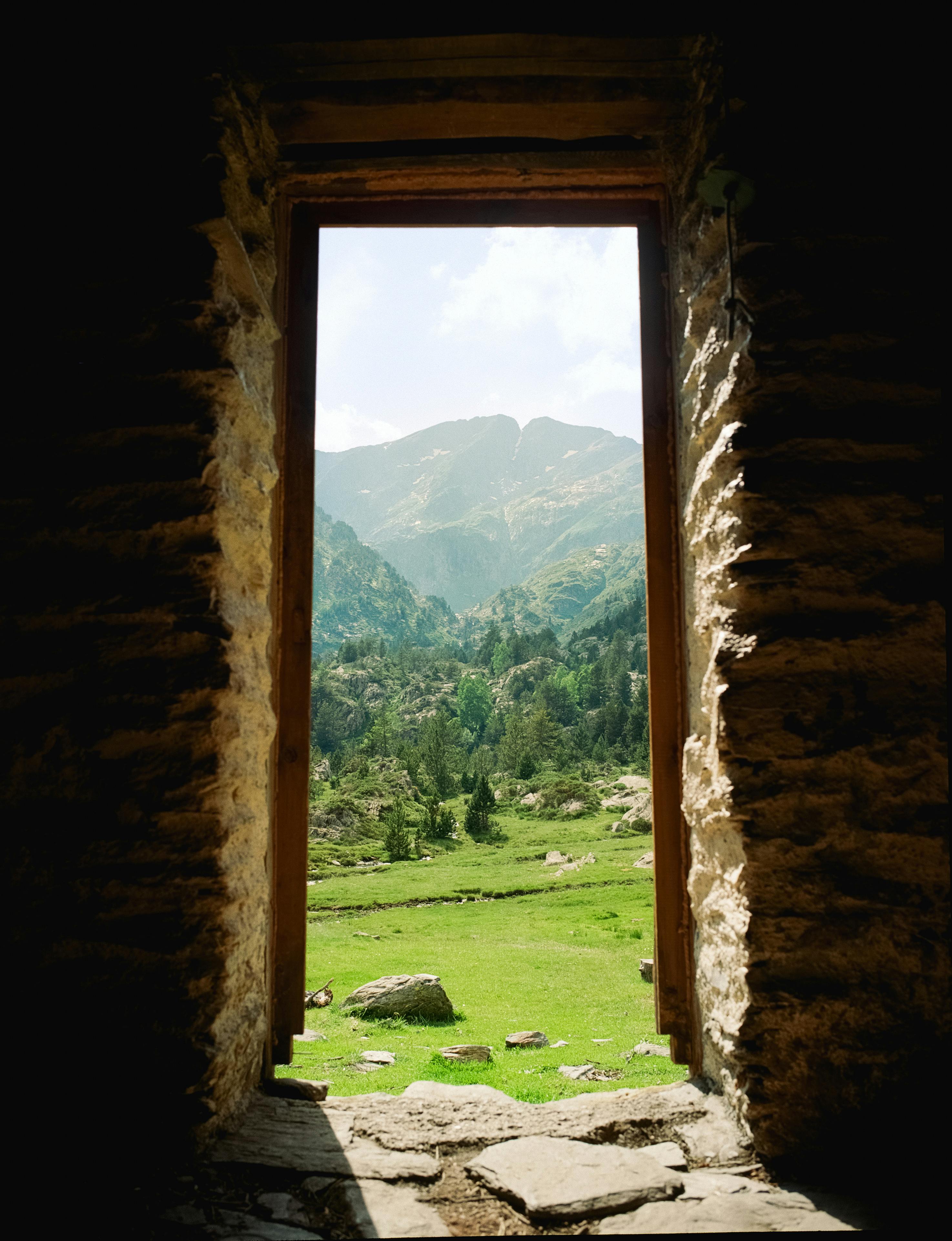 The view of green meadows and mountains framed by a rustic stone doorway.