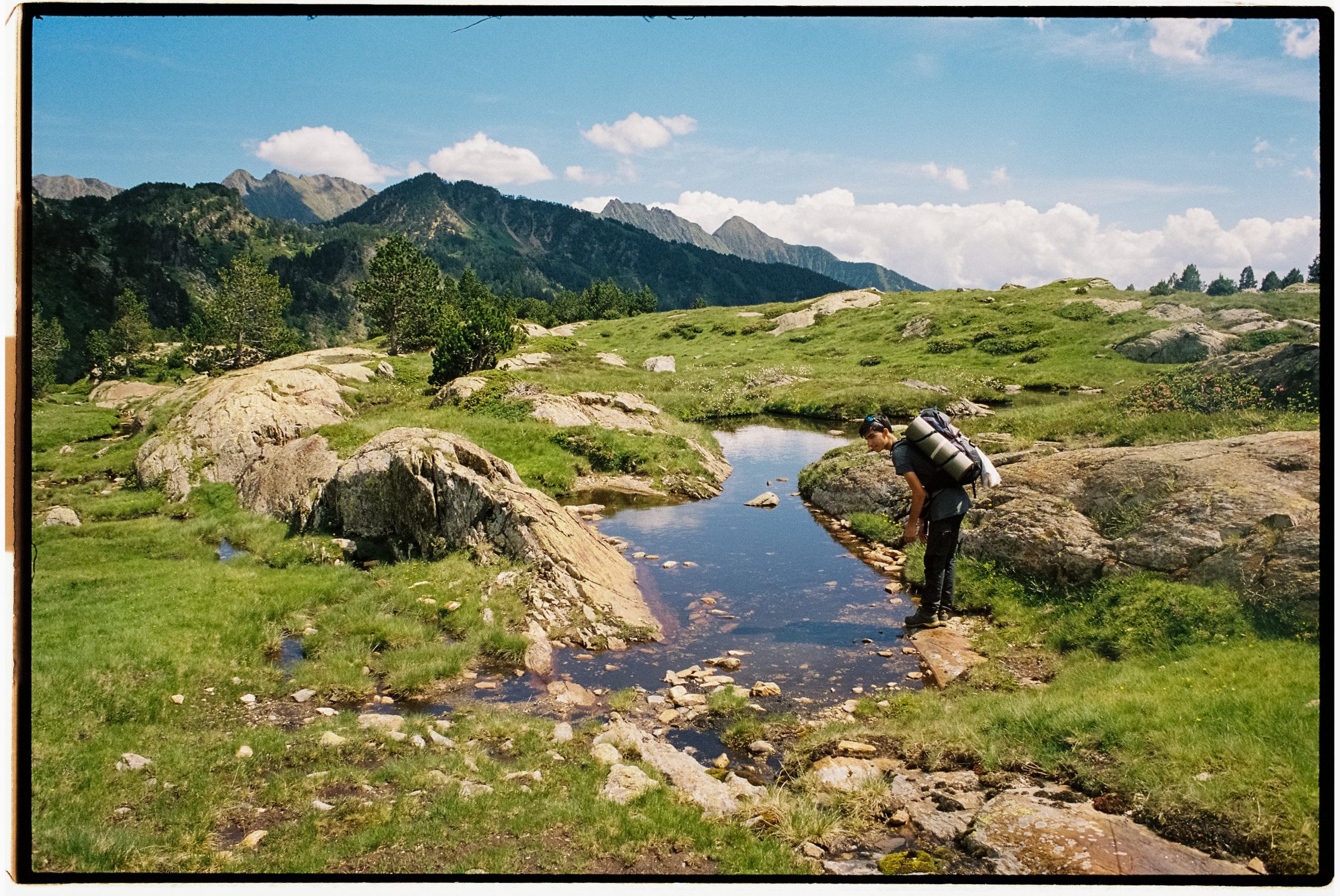 Backpacker crossing a serene mountain stream in a remote wilderness landscape Backpacker crossing a serene mountain stream in a remote wilderness landscape