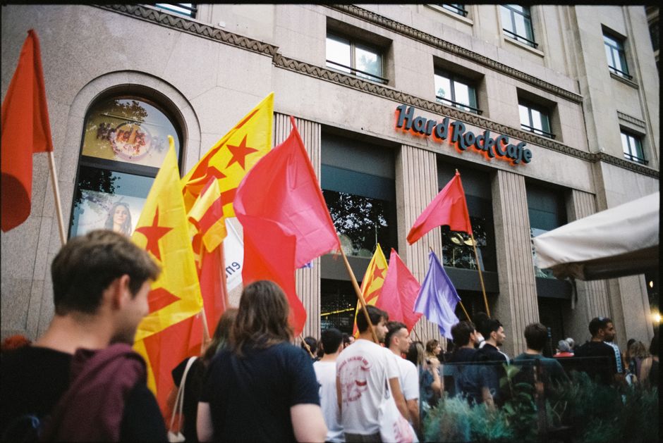 Un grupo de manifestantes ondeando banderas coloridas frente al Hard Rock Cafe en una calle de la ciudad durante el día.