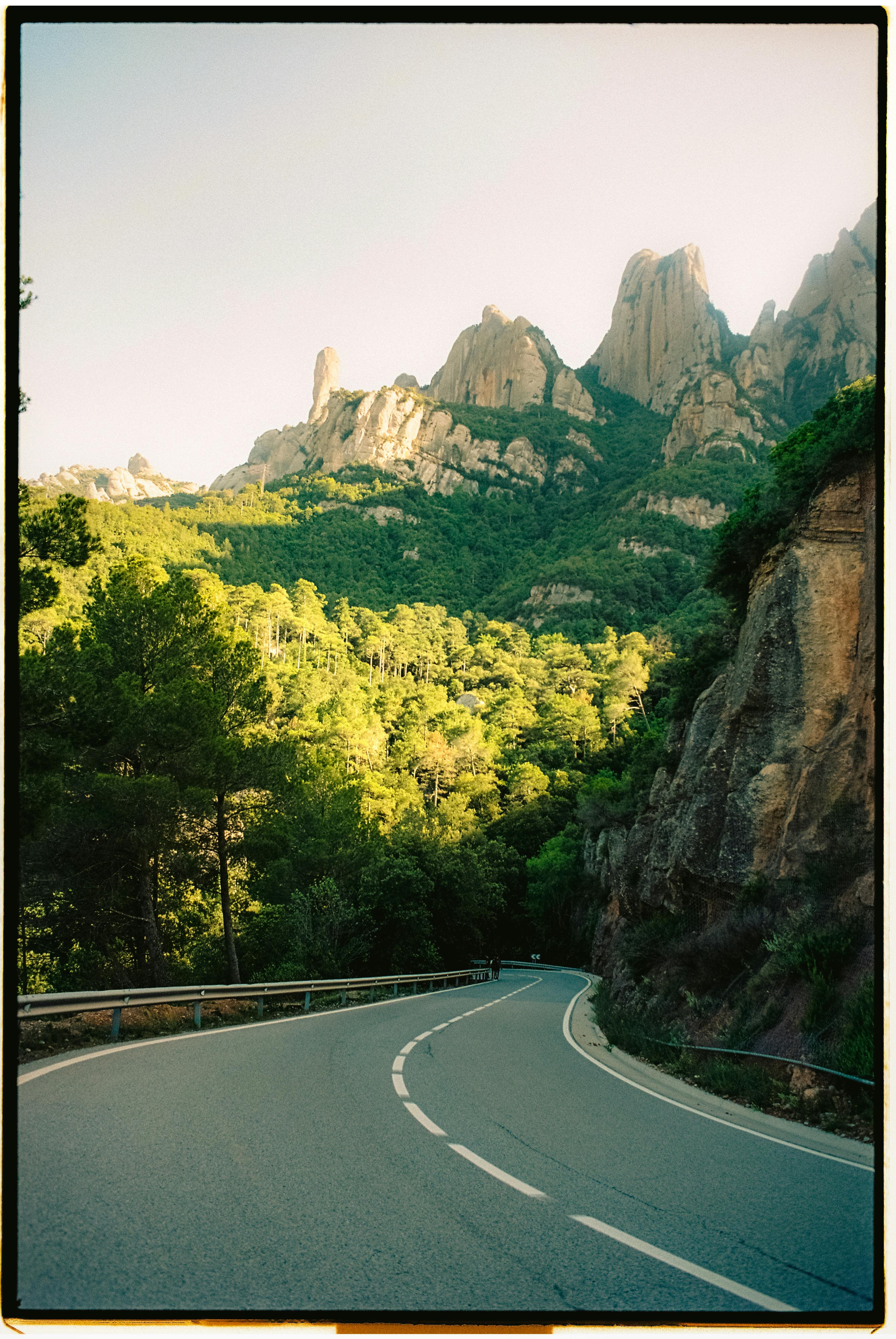 A winding road through lush forests against a backdrop of majestic mountain peaks in the summer sun.