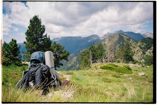 A lone hiker sitting with a backpack, enjoying a majestic mountain view under a summer sky.