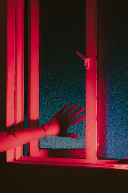 A creatively lit scene featuring a hand reaching towards a window with dramatic red and blue lighting.