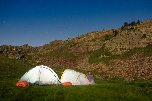 Tents in a serene mountain landscape under a starry night sky, showcasing a pristine camping experience.