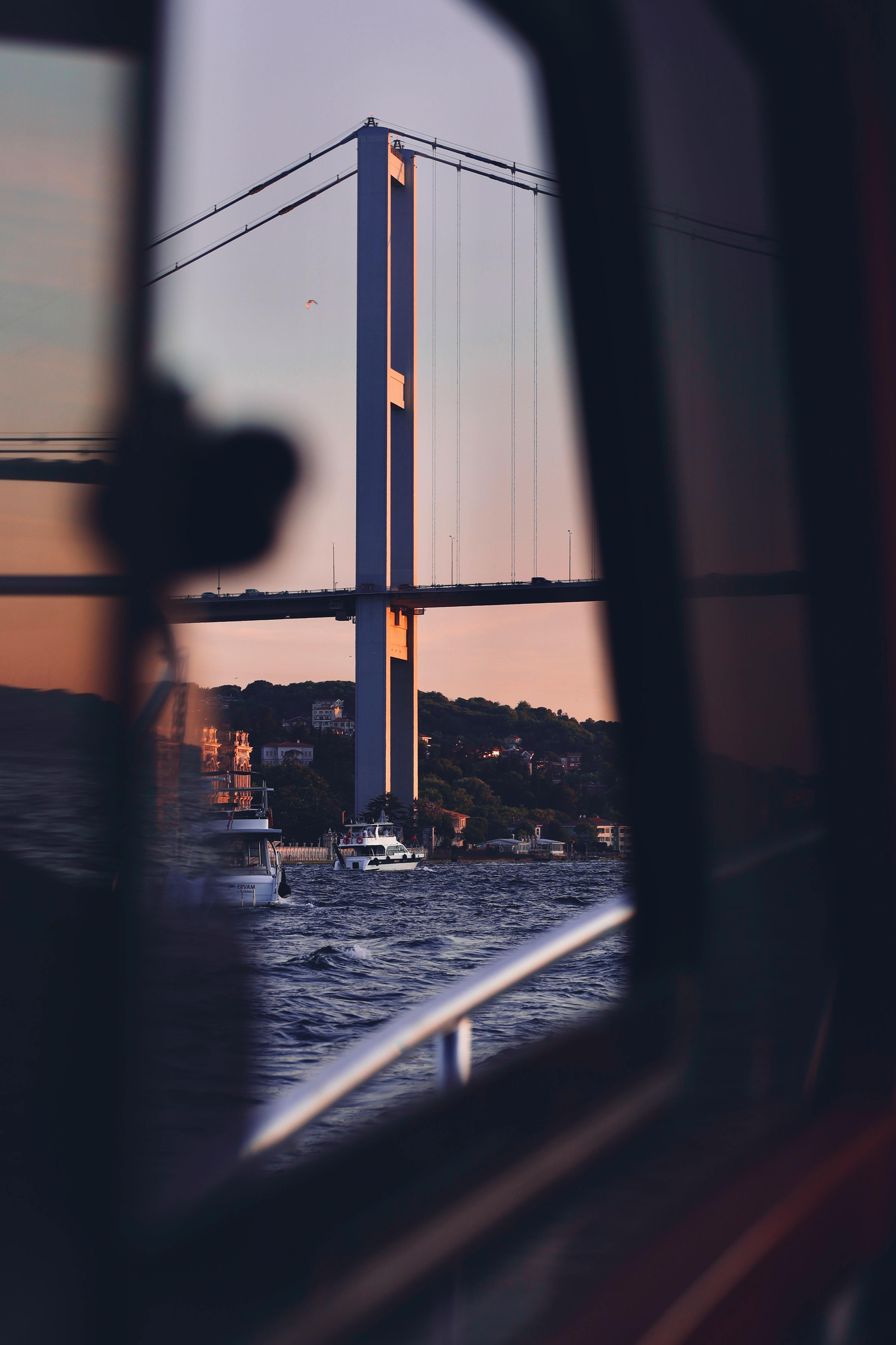 Capture of Bosphorus Bridge and Istanbul skyline at sunset, reflecting on the water.