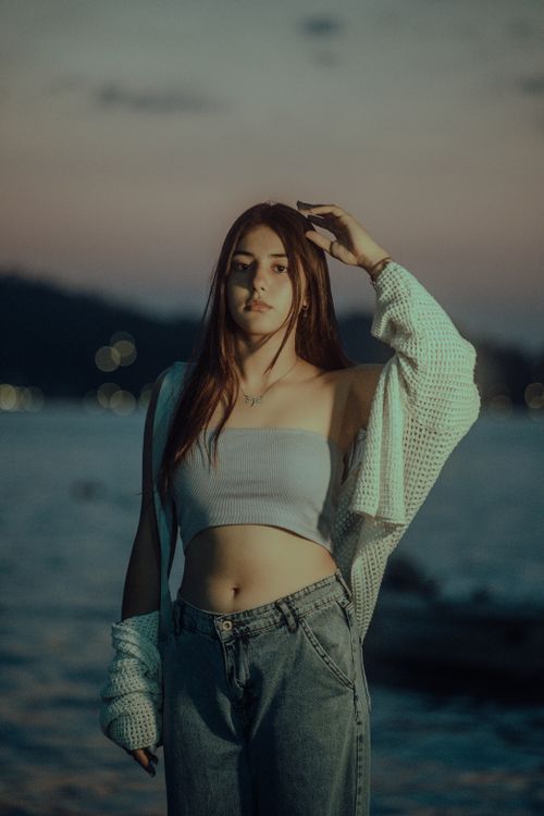 Free A stylish young woman stands by the sea during sunset, creating a serene and fashionable portrait. Stock Photo
