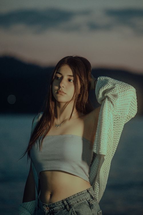 Free Beautiful woman in stylish outfit posing by the serene ocean during sunset, capturing elegance and tranquility. Stock Photo