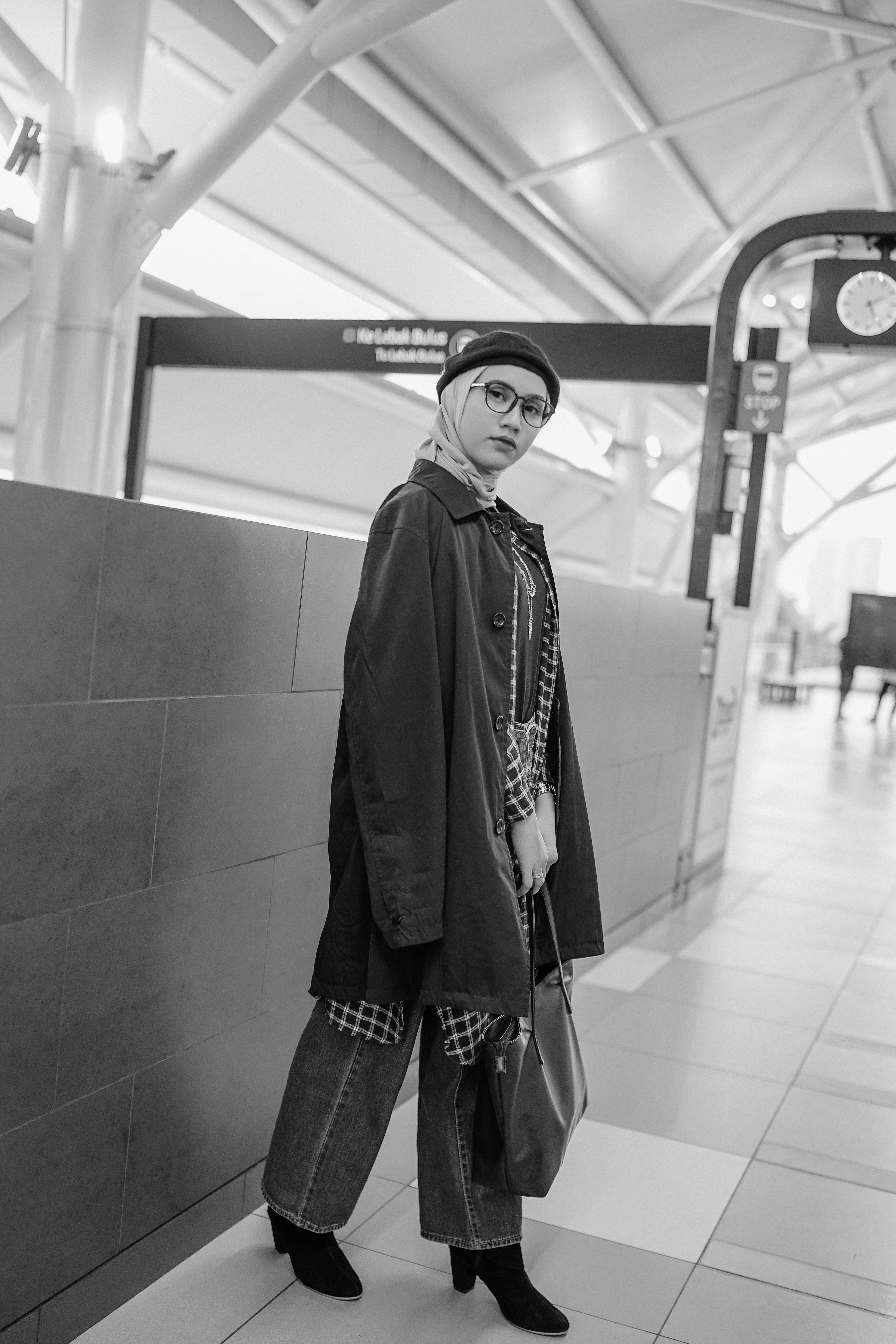 A fashionable woman stands indoors, showcasing her stylish outfit in a black and white photo.