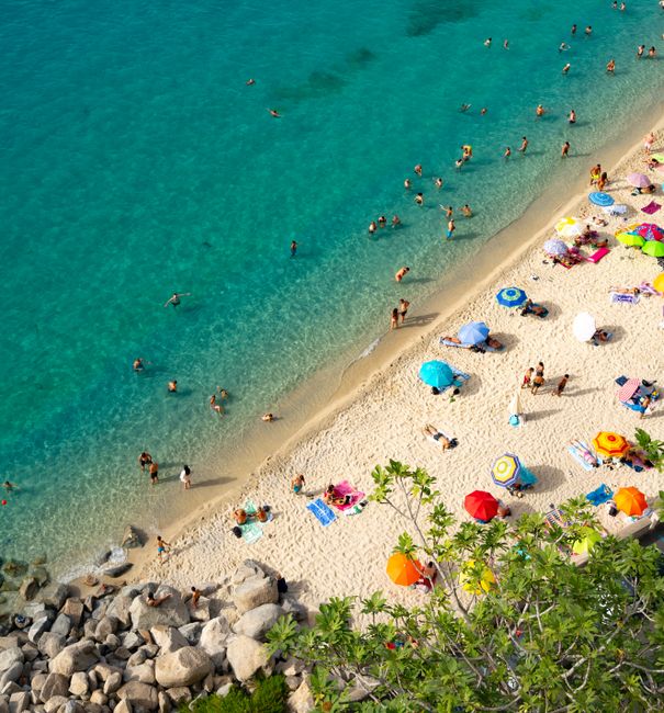 Vibrant beach scene at Tropea, Calabria, Italy with turquoise waters and colorful umbrellas.