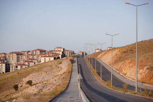 Free A modern urban landscape with a road winding through newly constructed apartment buildings under a clear sky. Stock Photo