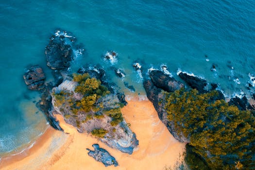 空中拍摄的沙滩绿松石水域被岩石悬崖环绕，景象令人惊叹