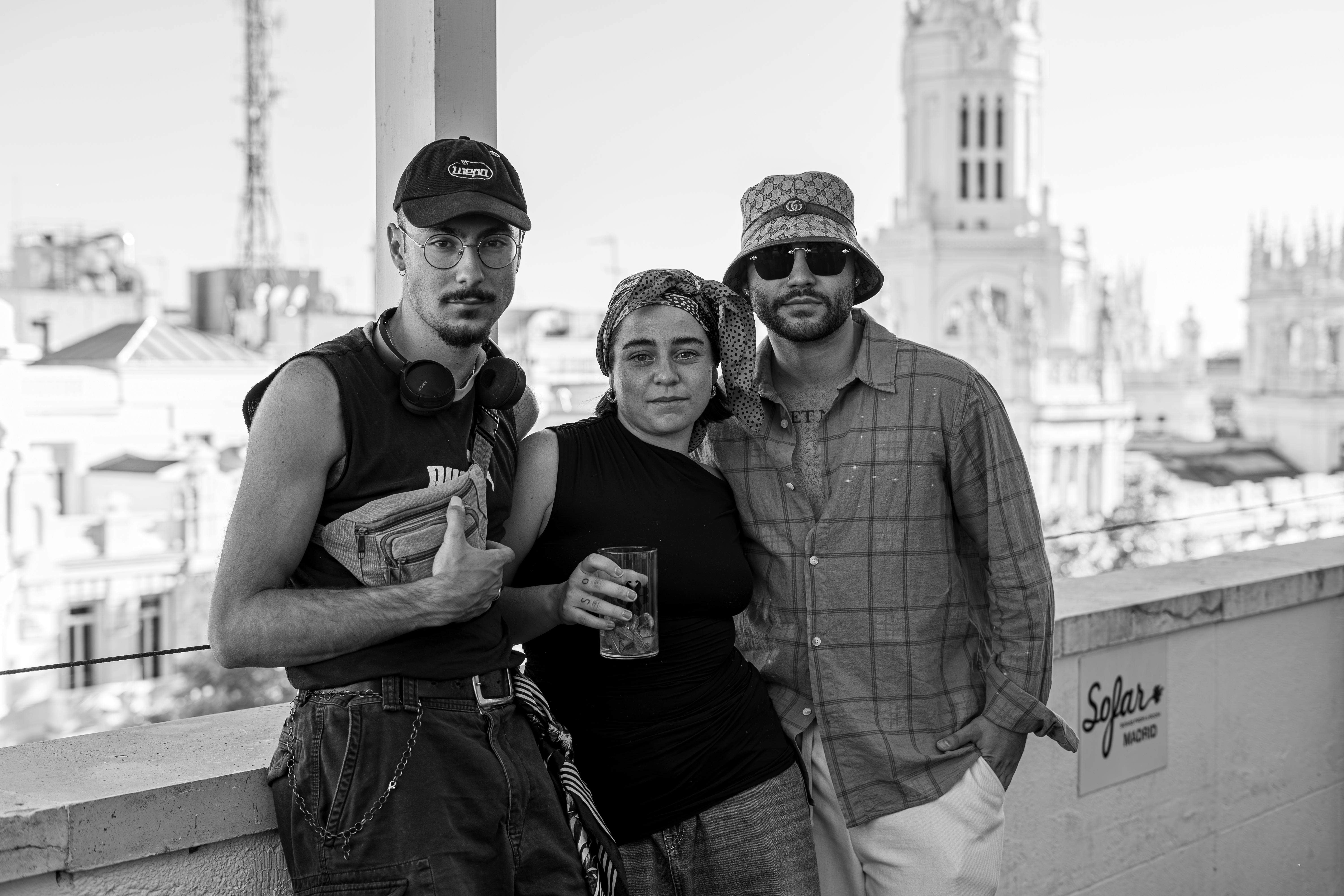 Black and white photo of three friends posing on a Madrid rooftop with a cityscape background.