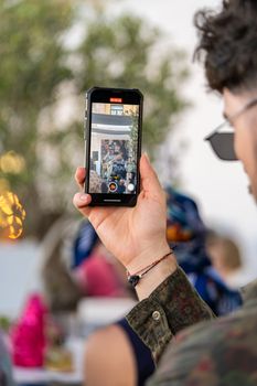 A man uses a smartphone to capture the vibrant urban festival scene outdoors.