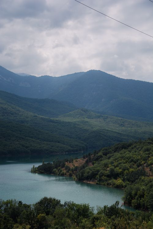 Free Serene landscape of a mountain lake surrounded by lush hills under a cloudy sky. Stock Photo
