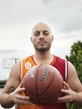 Bald basketball player holding a ball outdoors, showing determination.